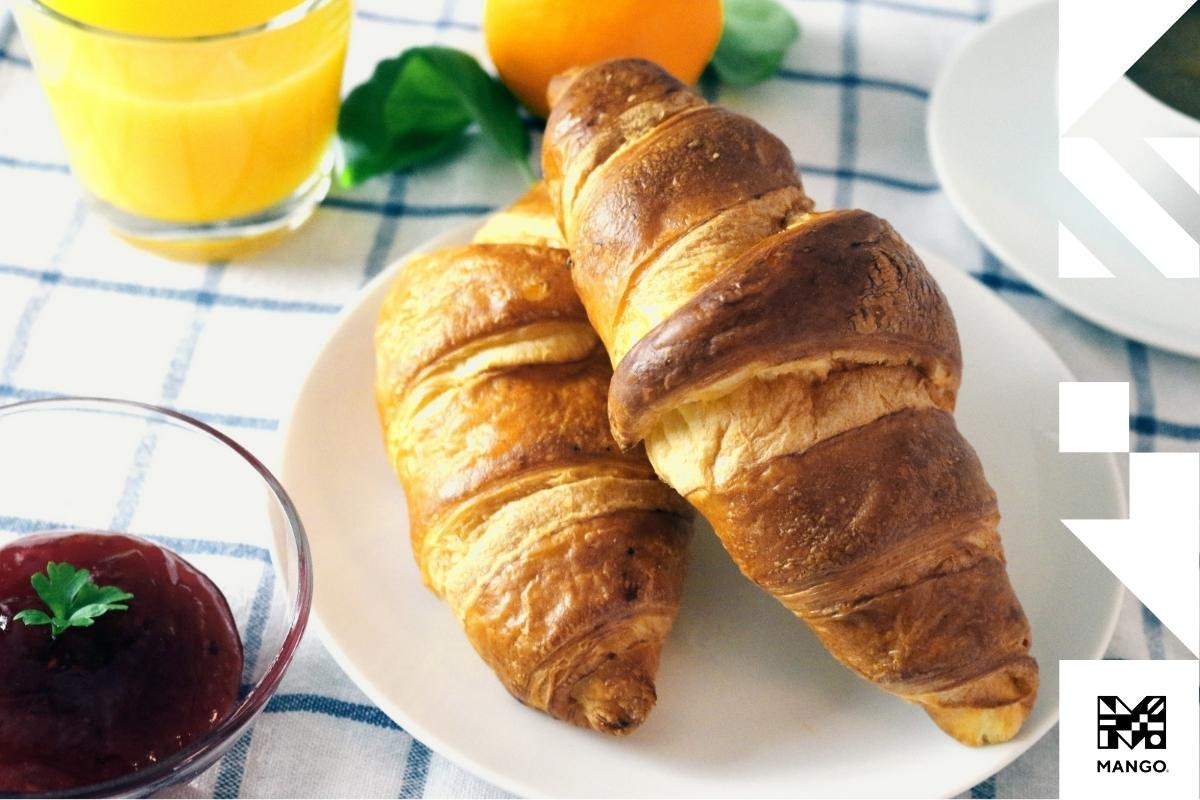 Two croissants displayed on a plate with a side of a jam and a glass of orange juice