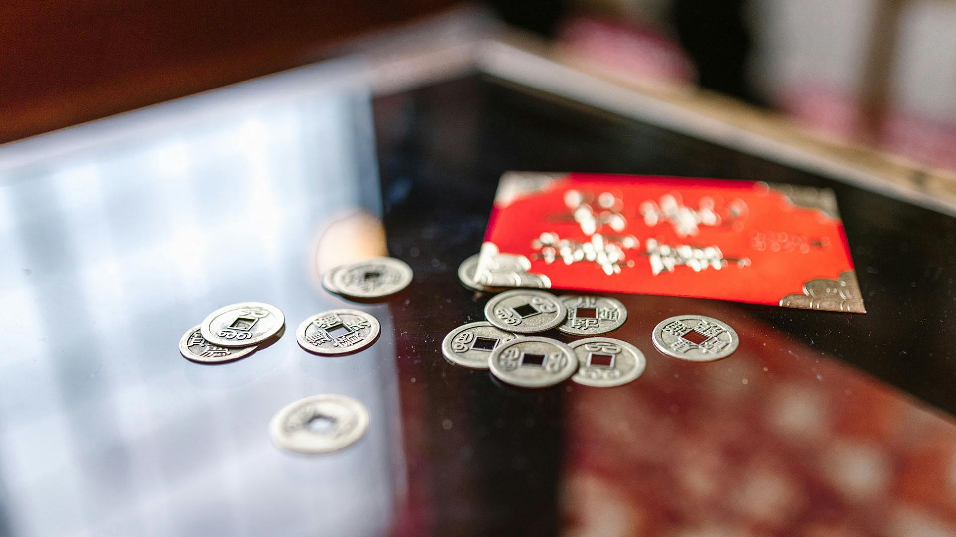 An red envelope with gold lettering on a glass table with a pile of old coins