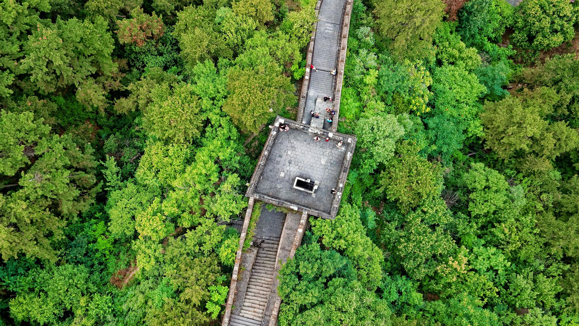 A view of a tower on the Great Wall of China from above. It's surrounded by a forest.