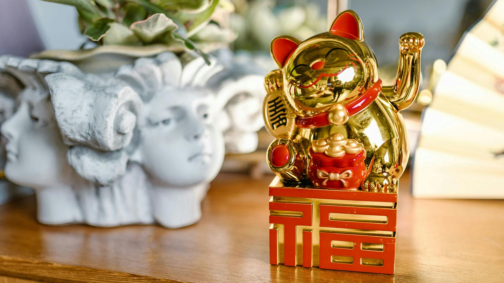 A lucky cat figurine on a shelf with some other tchotchkes like statuettes and hand fans